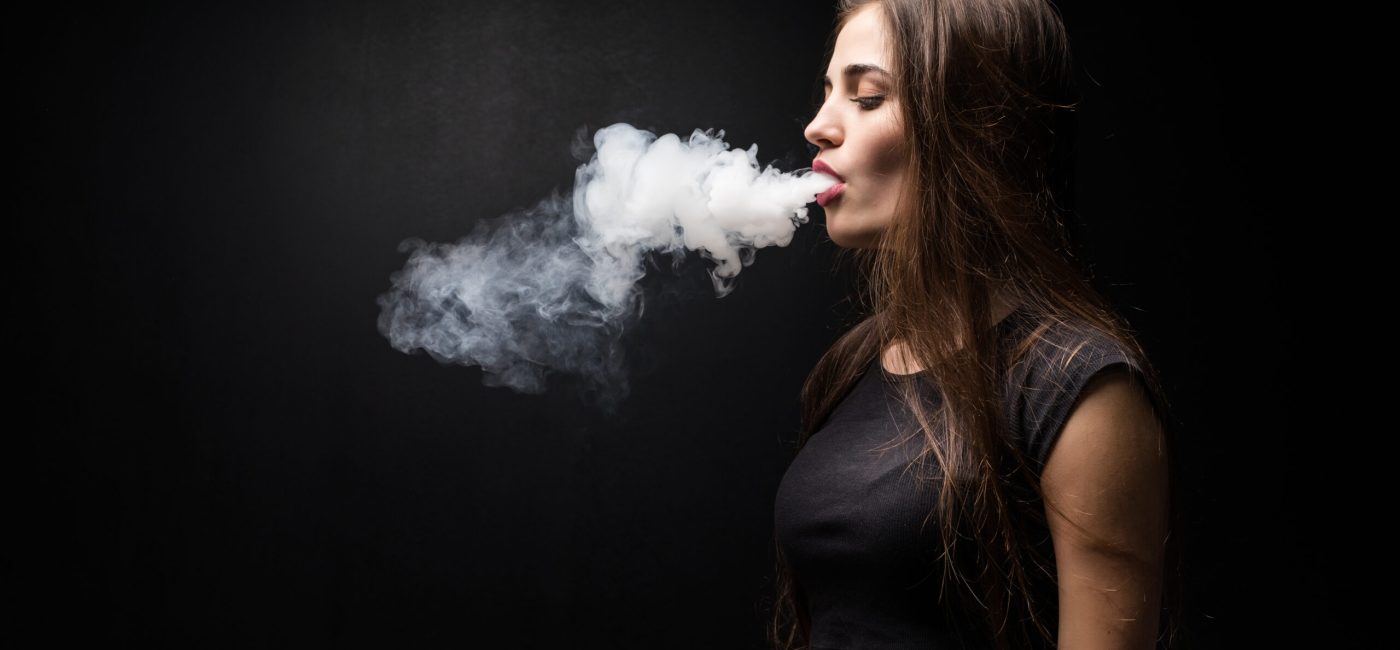 Young beautiful woman vaping e - cigarette. Black background.